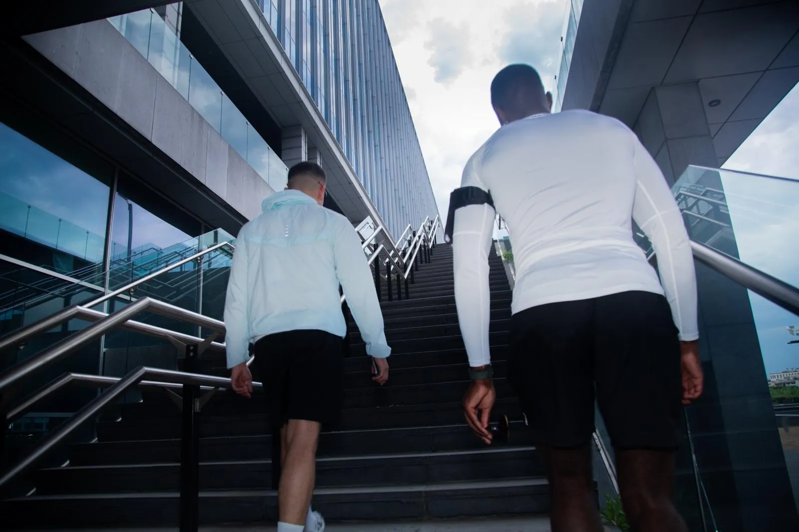 Two runners climbing outdoor stairs between office buildings, seen from behind