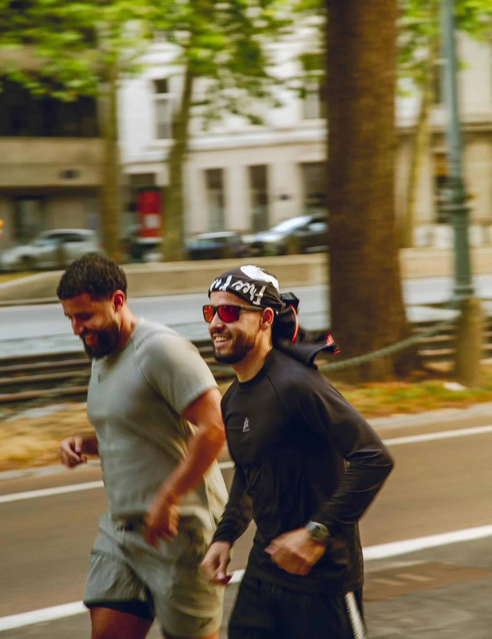 Two runners smiling mid-stride on a tree-lined avenue